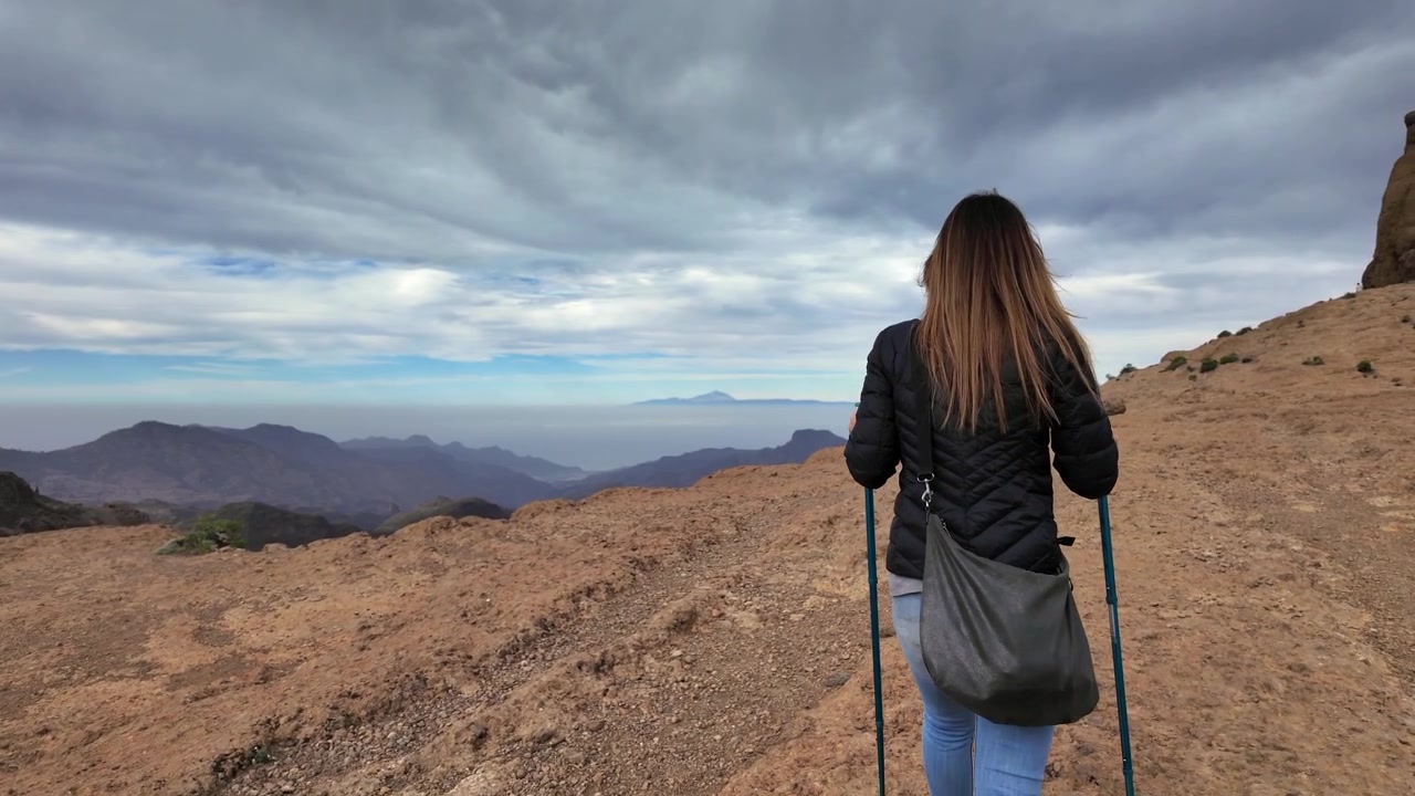 Donna con bastoncini da trekking che cammina su un sentiero di montagna. Splendida vista panoramica delle montagne di Gran Canaria