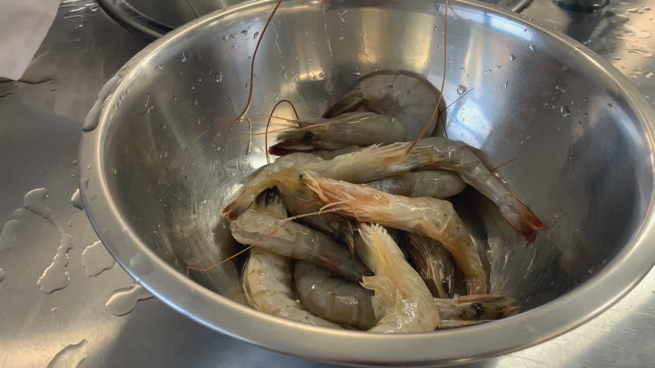 Stainless bowl full of large raw prawns in commercial kitchen meal prep