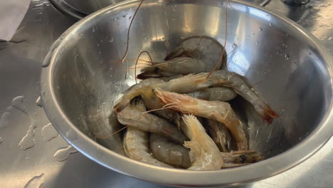 stainless bowl full of large raw prawns in commercial kitchen meal prep