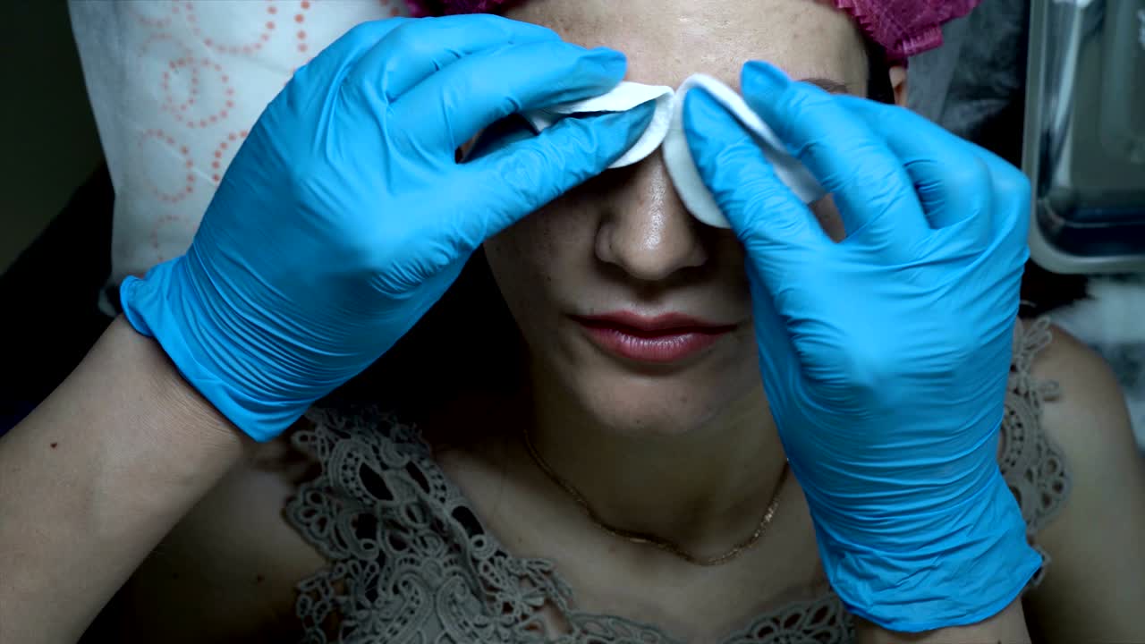The final result of the microblading procedure. A woman-cosmetologist wipes her eyebrows with a cotton swab to a young girl after permanent makeup of her eyebrows. The view from the top. 4K, 25 fps.
