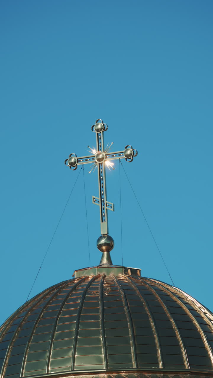 Elegant metallic church cross glowing under clear blue sky. Vertical