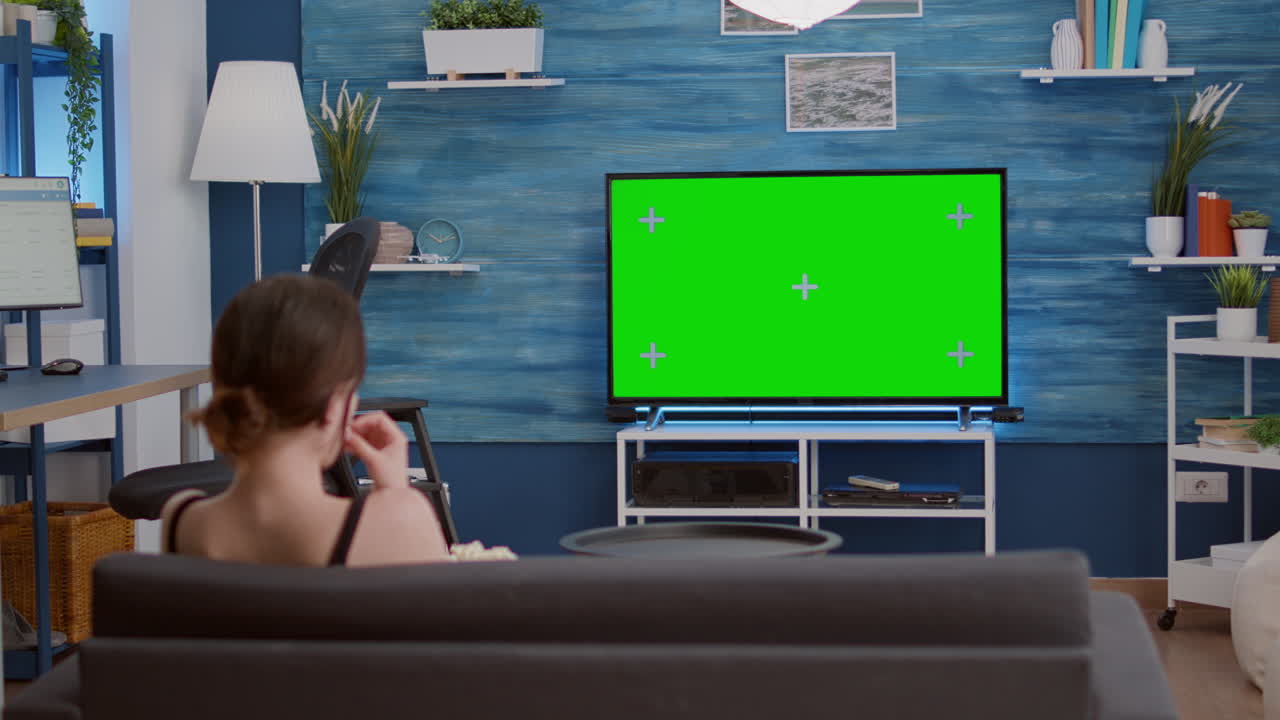 Young woman eating popcorn while relaxing watching movie on green screen television