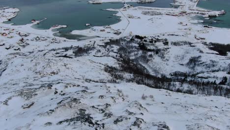 drone view in tromso area in winter flying over a snowy mountain peak and flat islands connected by bridges with small towns in norway