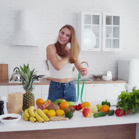 attractive girl with meter in the kitchen. fresh organic food on the table. young woman is measuring her waist at home. concept of losing weight.