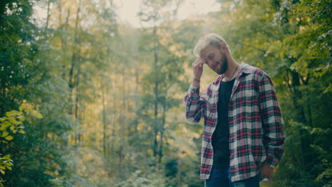 sad young man with head in hand standing in forest