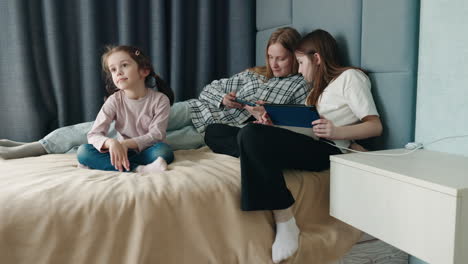 sisters and a little girl using digital devices in bedroom