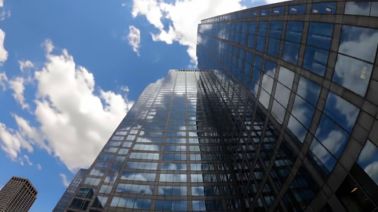 Gaze upward to admire the sleek glass architecture of skyscrapers under a bright blue sky. Stunning reflections and vibrant clouds create a beautiful cityscape full of life and energy.