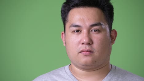 young handsome overweight asian man against green background