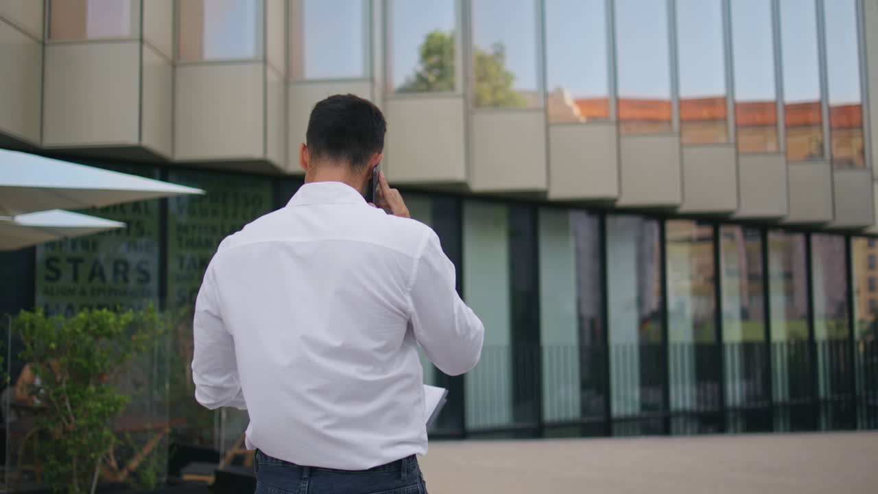 Successful entrepreneur making call walking in modern city back view. Man going