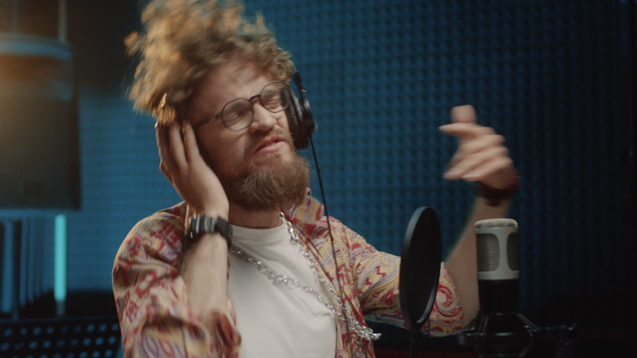 사운드 스튜디오에서 녹음하는 동안 마이크에서 감정적으로 노래하는 젊은 힙스터 세련되고 잘생긴 남자 가수