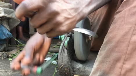 closeup shot of the hand of nigerian man sharpening a knife with a rolling grinding stone