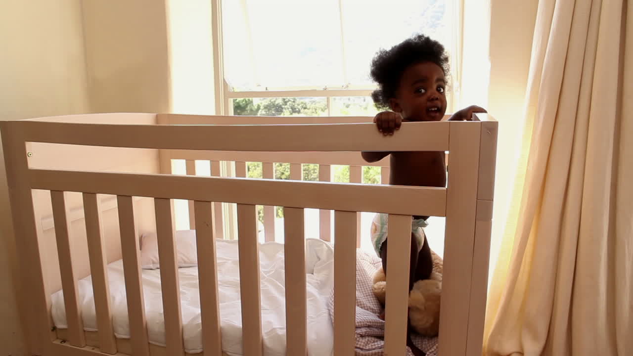 Bambina carina in piedi nella sua culla che guarda la telecamera