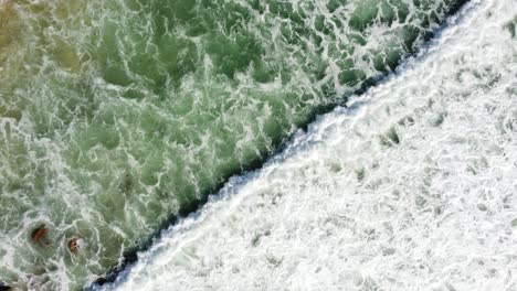 foamy ocean waves crashing on sandy beach, aerial top down view