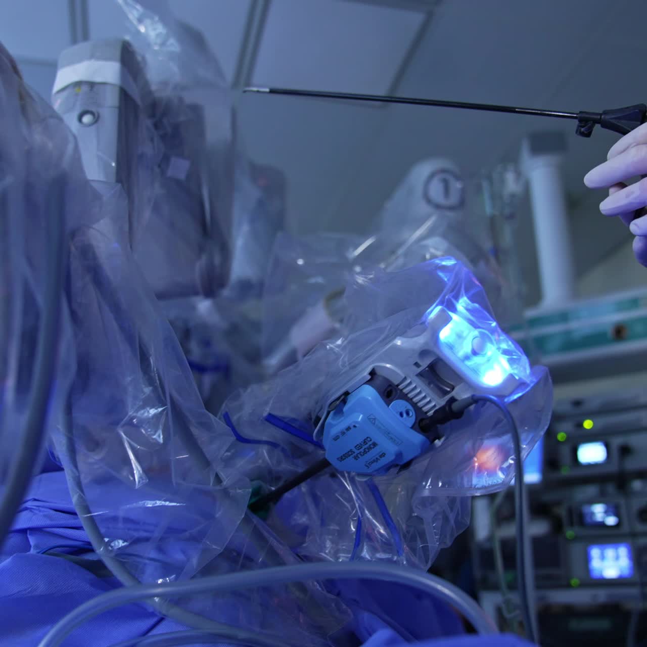 Doctor's hands in latex glove hold the surgical instrument for laparoscopy. Da Vinci robot performing modern surgery near the medic