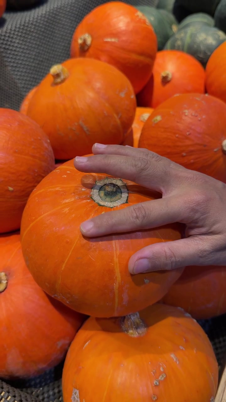 Hand Selecting Fresh Orange Pumpkins at a Grocery Store