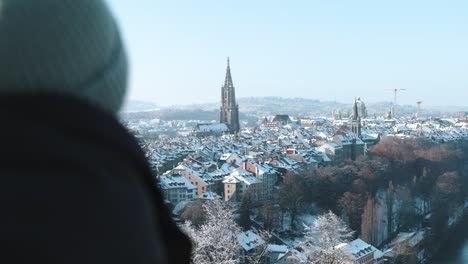 man looking at the view of the snow covered old town and cathedral in bern, switzerland during winter