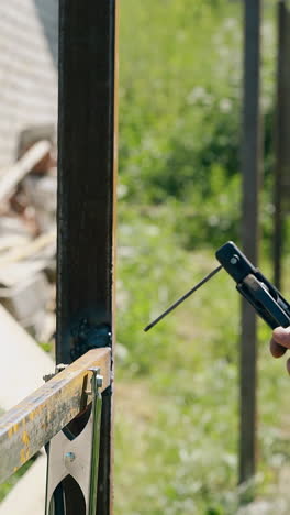 worker in camouflage welds metal fence with new tool at country house construction site closeup side view