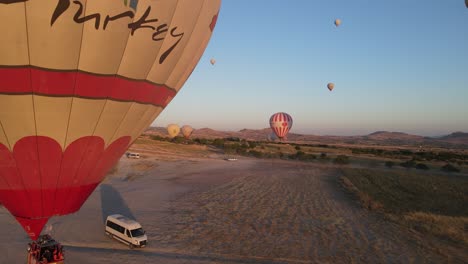 drone view of a colorful hot air balloon inflated on a wide plain, a very famous tourist attraction in cappadocia, turkey, the moment tourist vehicles approach the balloon