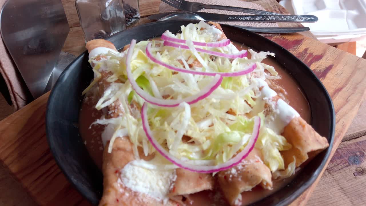 Overhead shot of enchiladas topped with cream, shredded lettuce, red onion, and served in bean sauce