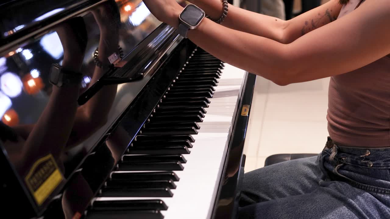 A woman in casual attire opens a grand piano lid and positions her hands to play, under bright indoor lighting with steady camera movement and close-up angles