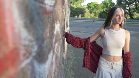 hermosa mujer joven caminando preocupada arrastrando su mano en la pared del parque al atardecer