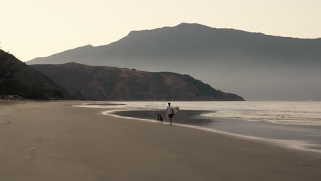 Surfer-Geht-Mit-Seinem-Hund-Am-Strand-Spazieren