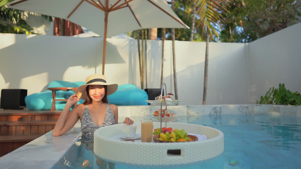 Attractive Asian woman in luxury pool with floating breakfast tray, vibrant