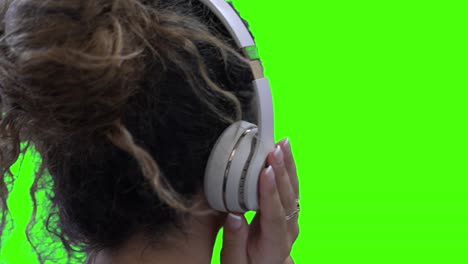 blonde woman with white headphones dancing to music, hand on side, green screen chroma key