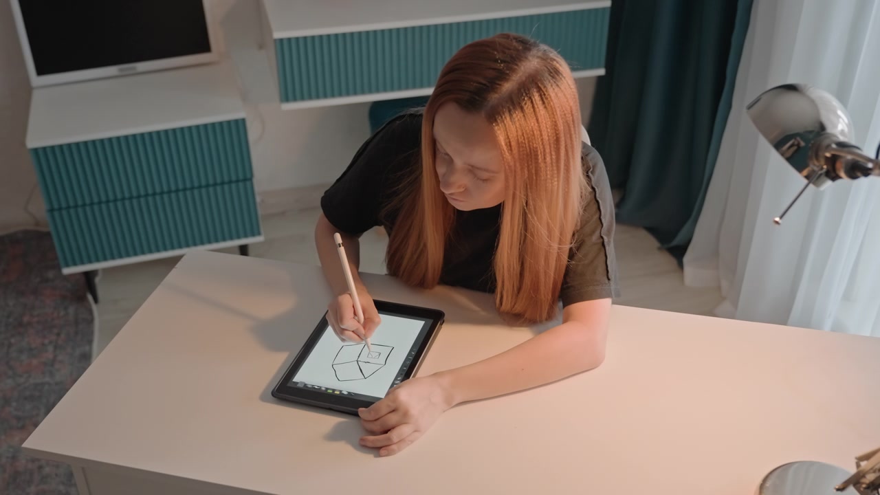 Jovem mulher com cabelo comprido desenha formas geométricas. A mulher veste uma blusa preta, cercada por um armário azul-petróleo, potes de vidro e um vaso de terracota. Um abajur de mesa é visível, e o ambiente é consistente.