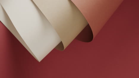 close up of three shades of brown rolled papers on red background with copy space in slow motion