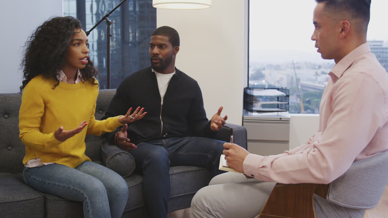 pareja infeliz sentada en el sofá reuniéndose con el consejero masculino en la oficina