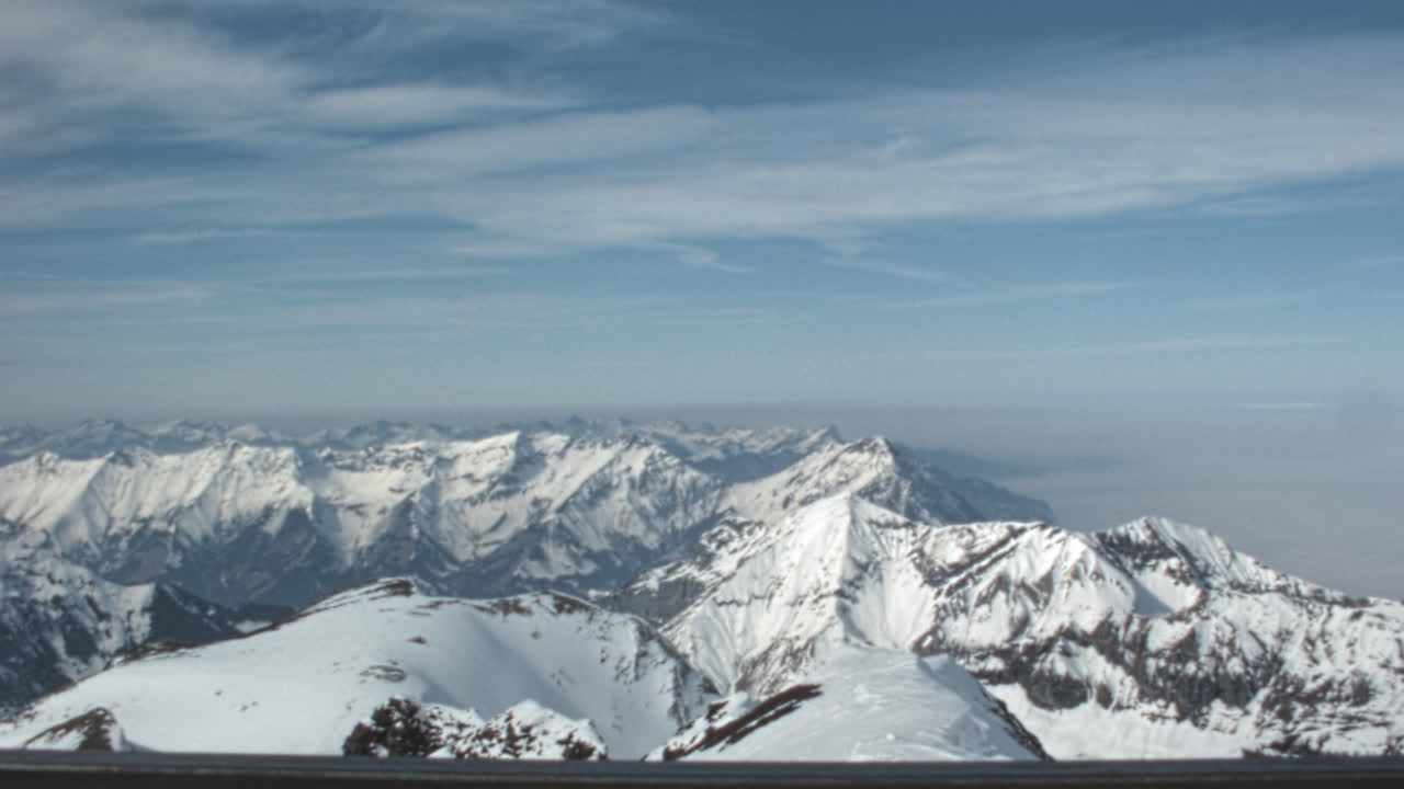Panorama of snow covered peaks of Swiss Alps above a sea of clouds, or nebelmeer. Archival footage shot from the Piz Gloria observation deck. Slow pan. Schilthorn Bernese Oberland Switzerland 1970s