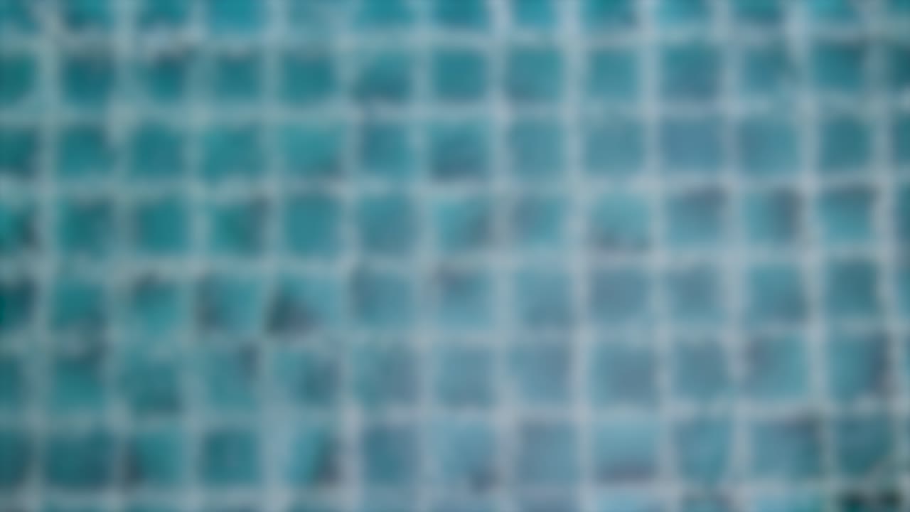 las gotas de lluvia crean ondas en una superficie de piscina azulejosa, capturadas en una secuencia de video serena y borrosa