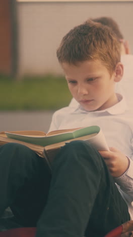concentrated pupil in white shirt does home assignment sitting on asphalt with school friends after lessons