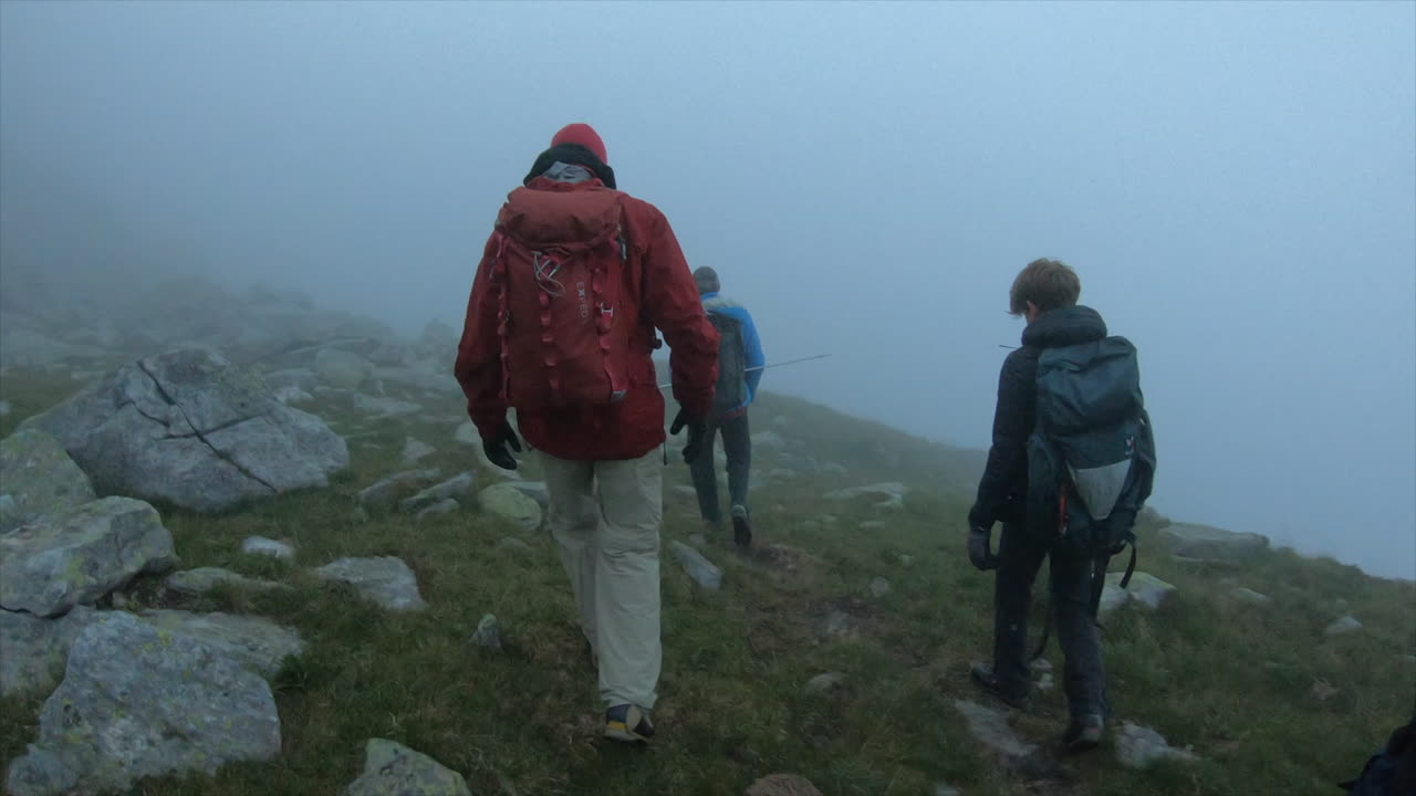 un grupo de alpinistas con mochilas se encuentran en una niebla matutina en un camino alpino por la mañana, alpes suizos