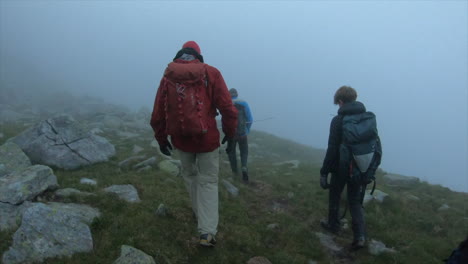 a group of mountain climbers with backpacks are in a morning fog on an alpine path in the morning, swiss alps