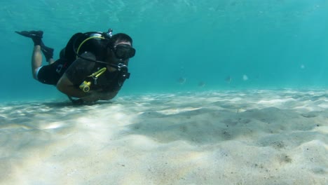 a scuba diver swimming along a sandy beach underwater