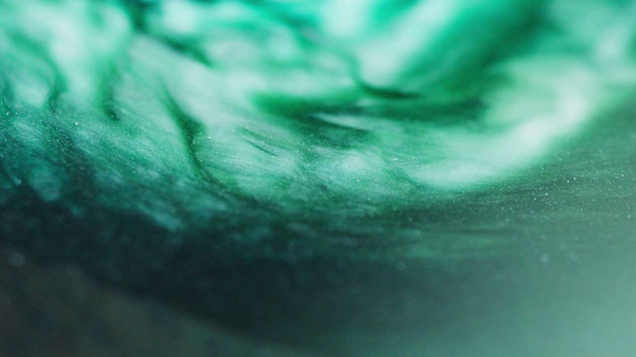 Macro shot of shiny green and white ink forming bubbles on the surface while in motion, with reflective highlights