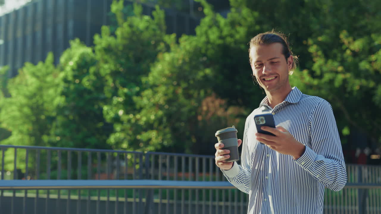 Smiling Man Using Phone and Holding Coffee Outdoors
