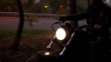 a man on a motorcycle rides among the trees with the headlight on in dusk