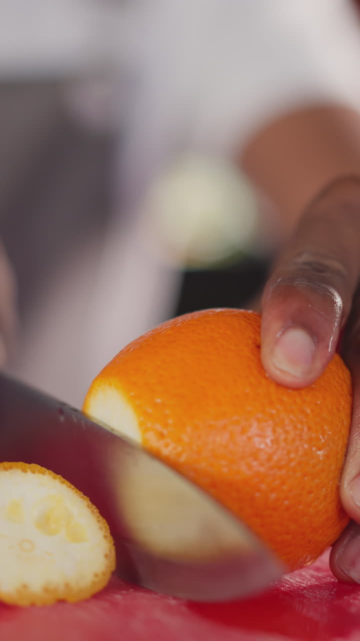 Black man cuts orange on table closeup. African American chef slices sweet citrus fruit for dessert cooking in kitchen. Natural exotic dish ingredient