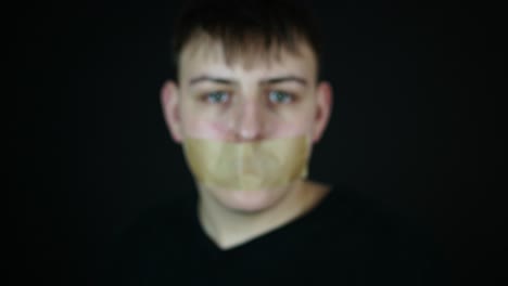 young man with tape covered mouth showing smartphone with green screen, internet censorship or cyber bullying concept