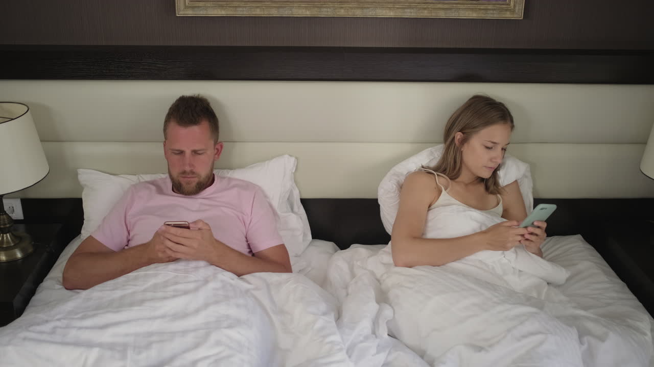 pareja en la cama, cada uno mirando sus teléfonos