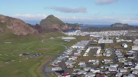 Isla-Nórdica-De-Heimaey-Con-Un-Pequeño-Pueblo-Remoto-Y-Un-Campo-De-Golf-Verde,-Antena