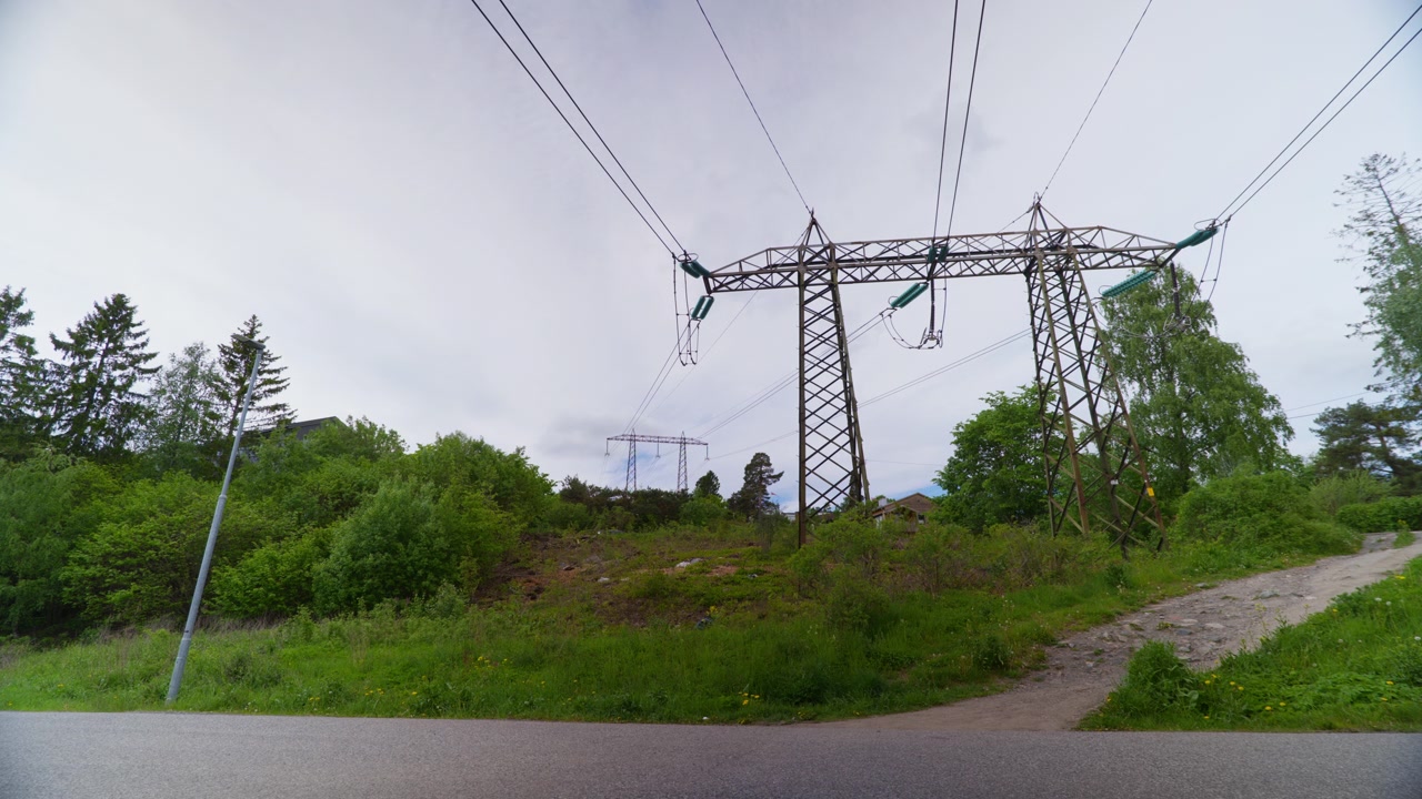 High-voltage power lines traverse a green landscape with trees and a clear sky. Suitable for energy infrastructure projects or environmental documentaries.