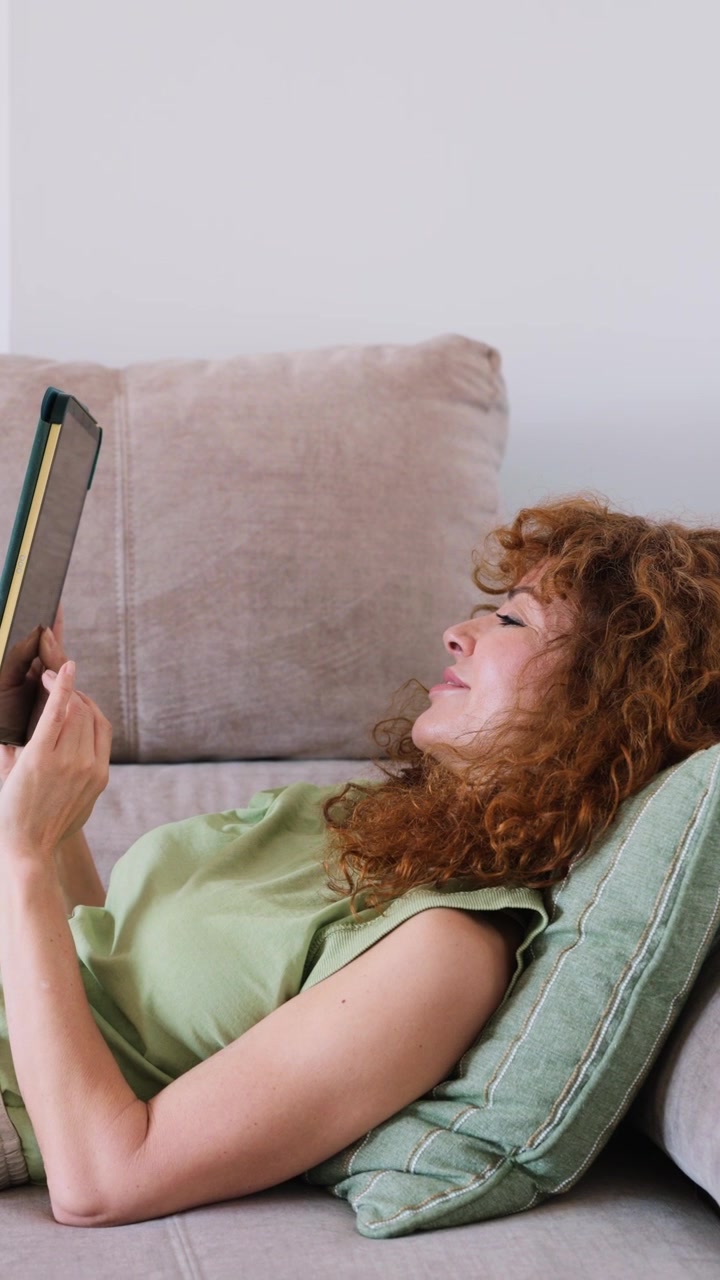 Donna matura che si rilassa sul divano e legge sul tablet