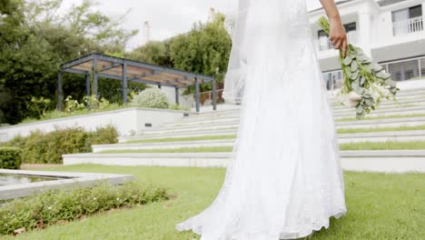 African-american-bride-walking-holding-bouquet-at-her-wedding-ceremony-in-garden,-in-slow-motion