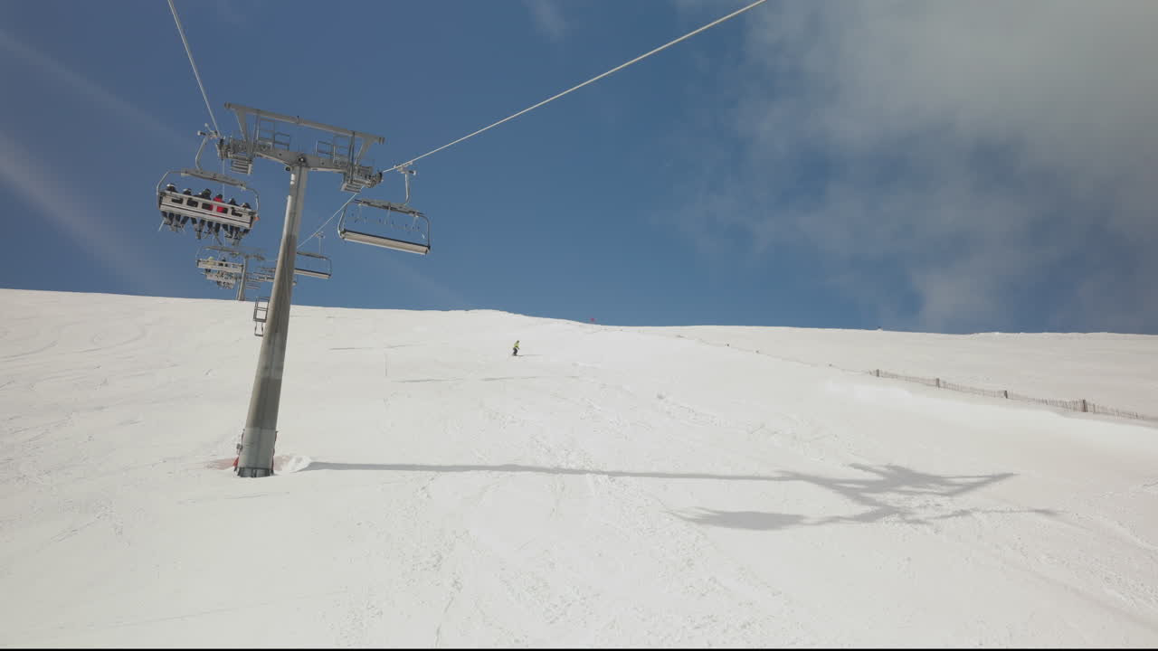 Sciatore che scende un pendio montano innevato con una seggiovia.