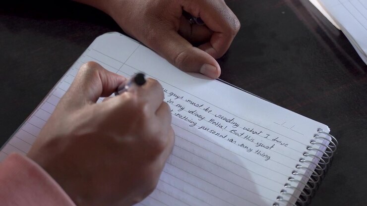 Close-up of a person writing by hand in a notebook at a desk, capturing a quiet moment of writing, planning, journaling, or personal reflection