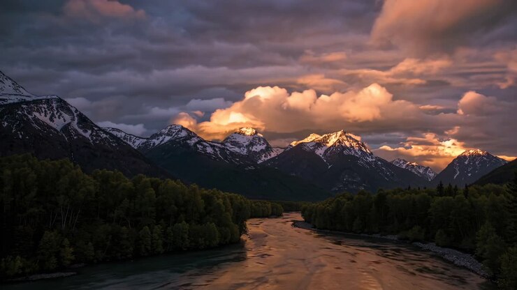 Video aereo che cattura un tramonto spettacolare su montagne innevate e un fiume tortuoso
